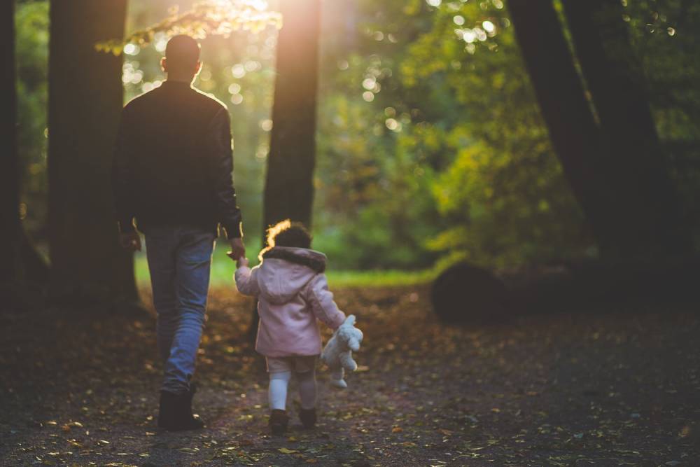 A father holds the hand of his young daughter as they take a walk through the forest