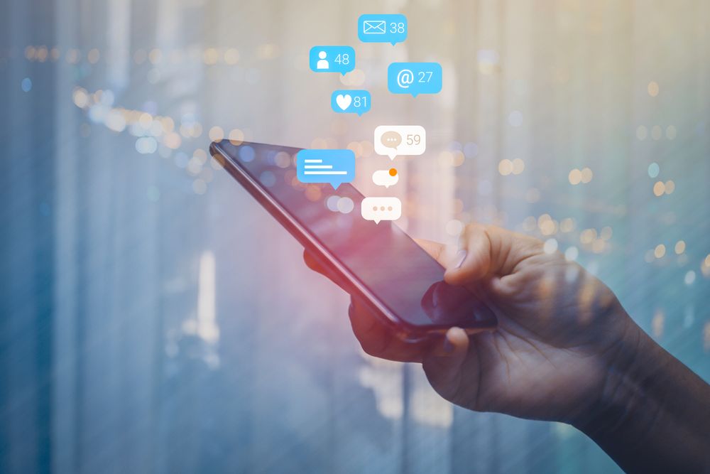 A woman holding an iPhone with social media icons emerging from it